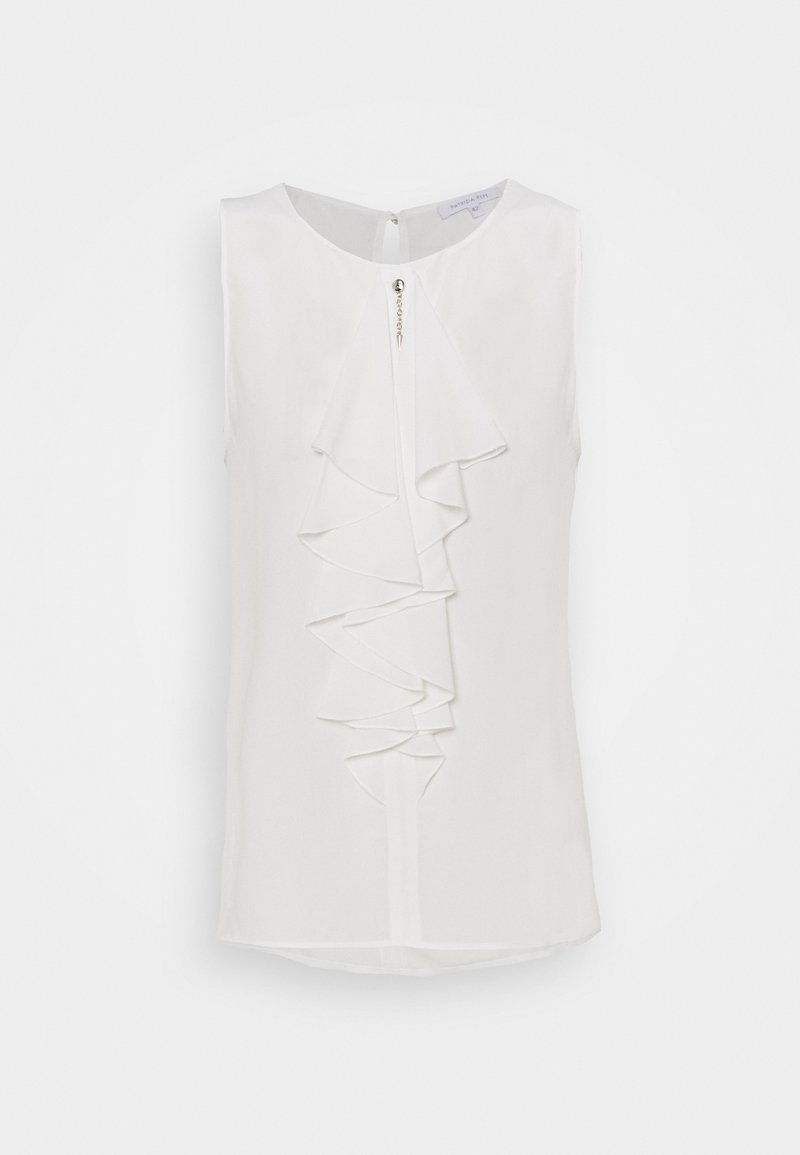 Blouse blanche sans manches avec volant superposé à l'avant et petit bouton décoratif à l'encolure, présentée sur fond uni.