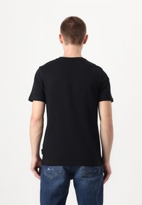 T-shirt noir à manches courtes avec col rond, fabriqué en coton, associé à un jean en denim bleu. Design simple, sans motifs ni graphiques visibles.