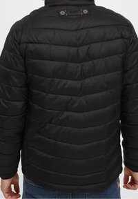 Zwarte gewatteerde jas met een quilted ontwerp, voorzien van twee bovenste knopen en een subtiele merklabel op de achterkant van de nek.