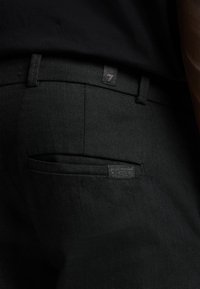 Zwarte broek met een soepele textuur, voorzien van een achterzak en een label met merkdetails nabij de tailleband.