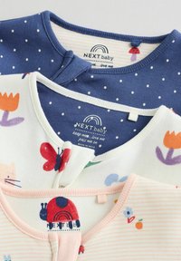 Tre babytröjor: marinblå med vita prickar, krämfärgad med blommor och fjärilar, samt rosa randig med en nyckelpiga som accent. Bomullstyg.