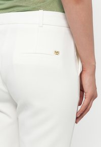 Witte op maat gemaakte broeken met een gladde textuur, voorzien van een enkele achterzak en een kleine gouden logo-accent.