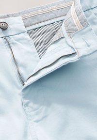 Vaaleansiniset housut, joissa on vetoketjukiinnitys, nappisuljenta ja raidallinen sisävuori. Housuissa on siistit saumat ja pehmeä, sileä pinta.