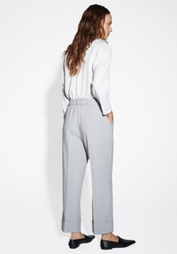 Hellgraue Hose mit entspannter Passform, ausgestattet mit einem elastischen Bund und umgekrempelten Säumen. Kombiniert mit einer weißen Bluse mit langen Ärmeln und schwarzen Schuhen.