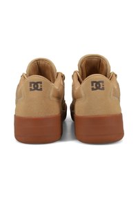 Tan-farbene Wildleder-Skate-Schuhe mit Gummisohle, gepolsterten Kragen, Logo-Akzent an der Ferse und glatter Textur.