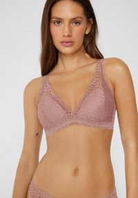 Krajkový bralet v tlumené mauve barvě s vlnkovaným lemem, vyrobený z jemné texturované tkaniny a s trojúhelníkovým designem košíčků. Bez kostice.