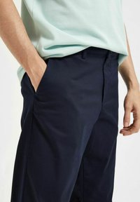 Navy blue trousers made of soft fabric, featuring a flat front, side pockets, and a slim fit. Minimal detailing on waistband.