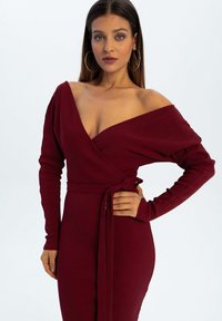 Bordowa sukienka w stylu wrap wykonana z żebrowanej tkaniny, z długimi rękawami i wiązanym w pasie, z dekoltem odsłaniającym ramiona dla dodatkowego efektu.
