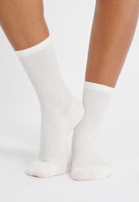 Calze bianche a coste con superficie testurizzata, caratterizzate da un colore uniforme e un design informale. Il bordo è leggermente arrotolato nella parte superiore.