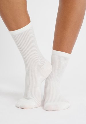 Calze bianche a coste con superficie testurizzata, caratterizzate da un colore uniforme e un design informale. Il bordo è leggermente arrotolato nella parte superiore.