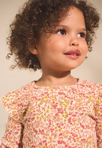 Lillemustriga kleit, millel on hele roosa alus ning oranžid, rohelised ja punased lilled, tekstureeritud kangas ja volangsete varrukatega.