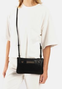 Zwarte leren schoudertas met een textuuraccent van gaas, slanke rechthoekige vorm en verstelbare schouderband. Voorzien van hardwareaccenten in goudkleur.