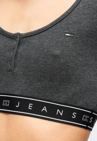 Γκρι κορμάκι από rib ύφασμα με στρογγυλή λαιμόκοψη, που διαθέτει λεπτομέρεια με κουμπί και μαύρη ταινία με την επιγραφή «JEANS» σε λευκά γράμματα.