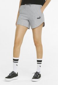 Šedé sportovní šortky s šňůrkou v pase, nesoucí černé logo Puma a zaoblený lem. Vybavené černými teniskami a pruhovanými ponožkami.