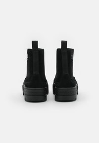 Bottes cheville en daim noir avec semelle noire épaisse, panneaux élastiques sur les côtés et boucles d'extraction à l'arrière. Texture lisse et détails minimaux.