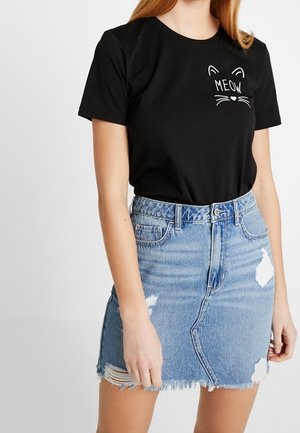 Czarna bawełniana koszulka z białym nadrukiem "MEOW" z detalami w kształcie kociej twarzy, zestawiona ze jasnoniebieską dżinsową spódnicą z postrzępionym dołem i przetartymi sekcjami.