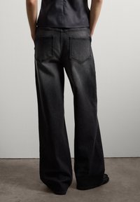 Jeans de mezclilla oscura de pierna ancha con una textura desvanecida. Presentan bolsillos traseros y un ajuste holgado, combinados con una parte superior elegante y ajustada.