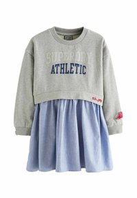 Szürke pulóver "SUPERDRY ATHLETIC" felirattal, kék chambray szoknyával párosítva. Bordás mandzsettákkal és egy ujján folttal rendelkezik.
