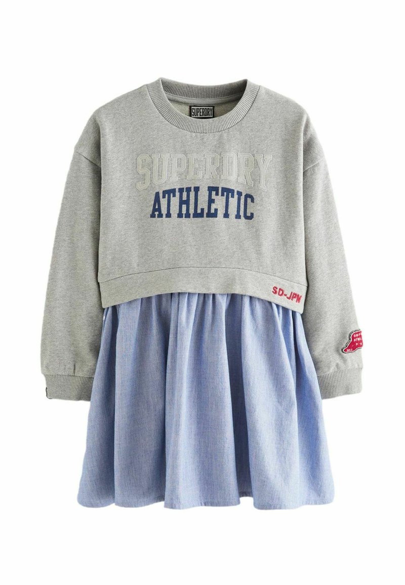 Szürke pulóver "SUPERDRY ATHLETIC" felirattal, kék chambray szoknyával párosítva. Bordás mandzsettákkal és egy ujján folttal rendelkezik.