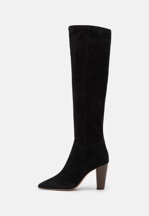 Botte noire en daim montant jusqu'au genou, avec un bout pointu et un talon empilé. Texture lisse et design élégant ; la tige dépasse le mollet.