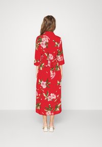 Abito lungo floreale rosso con maniche 3/4, dotato di una vita regolabile, fiori rosa e foglie verdi su un tessuto strutturato.