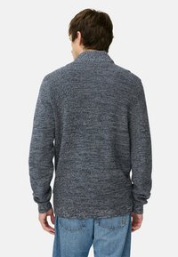 Donkergrijze, gestructureerde gebreide trui met een hoge kraag en lange mouwen, gecombineerd met lichtblauwe, loszittende jeans.