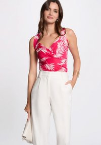 Top avvolgente rosa aderente con stampa di foglie di palma bianche, abbinato a pantaloni a vita alta color crema; tessuto morbido e spalline larghe.