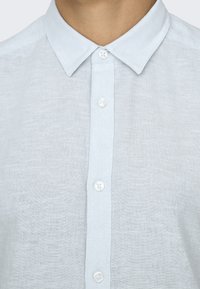 Jasnoniebieska lniana koszula zapinana na guziki z klasycznym kołnierzykiem, wyposażona w białe guziki i lekko teksturowaną tkaninę.