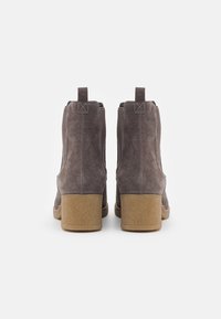 Bottines en daim gris avec une semelle épaisse beige, dotées de panneaux élastiques latéraux et de languettes pour un enfilage facile. Fini texturé.