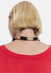 Gold and tortoiseshell bead necklace with glossy texture, worn with a red shirt, viewed from the back, highlighting the necklace’s design.