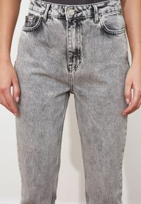 Vysoké šedé džíny z denimu s distressed akcenty, předními kapsami a slim straight leg střihem. Obsahují kovový knoflík a poutka na opasek.