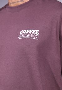 Rudas medvilnės marškinėliai su tekstu "KAVA HARMONIJA" balta spalva, su apvaliu kaklu ir minkšta tekstūra.