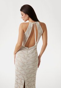 Strickkleid in hellbeige mit Zickzackmuster, offener Rückseite und einem Halterneck mit verstellbaren Bindebändern. Seitlicher Schlitz am Saum.