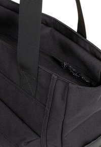 Czarna torba tote z materiału, z nylonowymi ramiączkami, zawierająca kieszonkę na zamek błyskawiczny i teksturowaną powierzchnię. Ustrukturyzowany design z wzmocnionymi szwami.