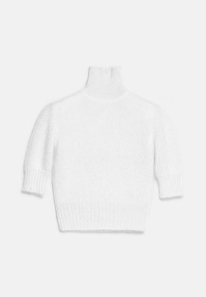 Femme portant un pull à col roulé blanc, une jupe midi noire texturée, une ceinture imprimé serpent, un sac assorti et des talons hauts, debout sur fond blanc.