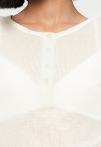 Λευκό, ριμπ πλεκτό τοπ με στρογγυλή λαιμόκοψη και πέντε διαφανή κουμπιά στο μπροστινό μέρος. Λείο ύφασμα και ελαφρύ, διαπνέον ύφασμα.