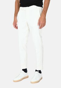 Pantaloni di velluto a coste bianchi con una vestibilità affusolata, caratterizzati da una vita piatta, tasche laterali e una texture a coste, abbinati a sneakers bianche.