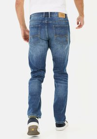 Męskie niebieskie dżinsy w prostym kroju, wyblakłym kolorze, z dwiema tylnymi kieszeniami i brązową skórzaną łatą na pasku. Casualowy design, klasyczny styl.