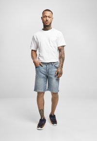 Hvid t-shirt med korte ærmer og lomme, lyseblue denimshorts med optrukket kant, og sorte sneakers med orange og lilla accenter.