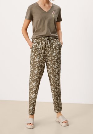Olive green V-neck t-shirt with floral embroidery; paired with patterned, drawstring, ankle-length pants in brown and off-white. Chunky beige sandals.