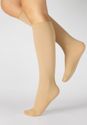 Medias altas de punto acanalado en color nude, que presentan una textura suave y elástica con un ajuste ceñido, acentuando la forma de las piernas.