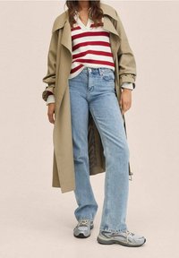 Trench-coat beige, pull à col en V rayé rouge et blanc, jean droit bleu clair, et baskets grises avec panneaux en maille.