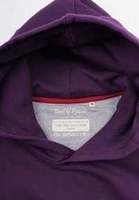 Sudadera de algodón morada con una textura suave, que presenta un forro interior gris y una etiqueta que detalla la certificación orgánica y las instrucciones de cuidado.