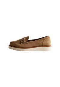 Chaussure à enfiler en suédine marron avec une sangle décorative et un détail de boucle, dotée d'une semelle en caoutchouc blanc et d'un design à bout arrondi.