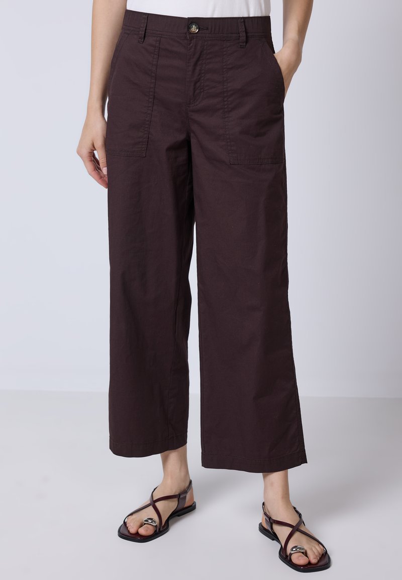 Pantalon large, bordeaux foncé en tissu léger. Avec poches avant et bouton de fermeture. Assorti avec des sandales plates noires.