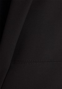 Gros plan d'un tissu noir avec une texture fine et une couture droite visible le long d'une couture horizontale.
