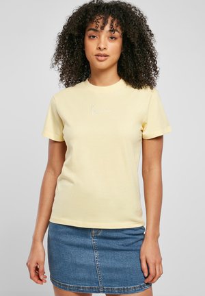 T-shirt en coton jaune à manches courtes, avec un logo brodé blanc sur la poitrine. Porté avec une jupe en denim.
