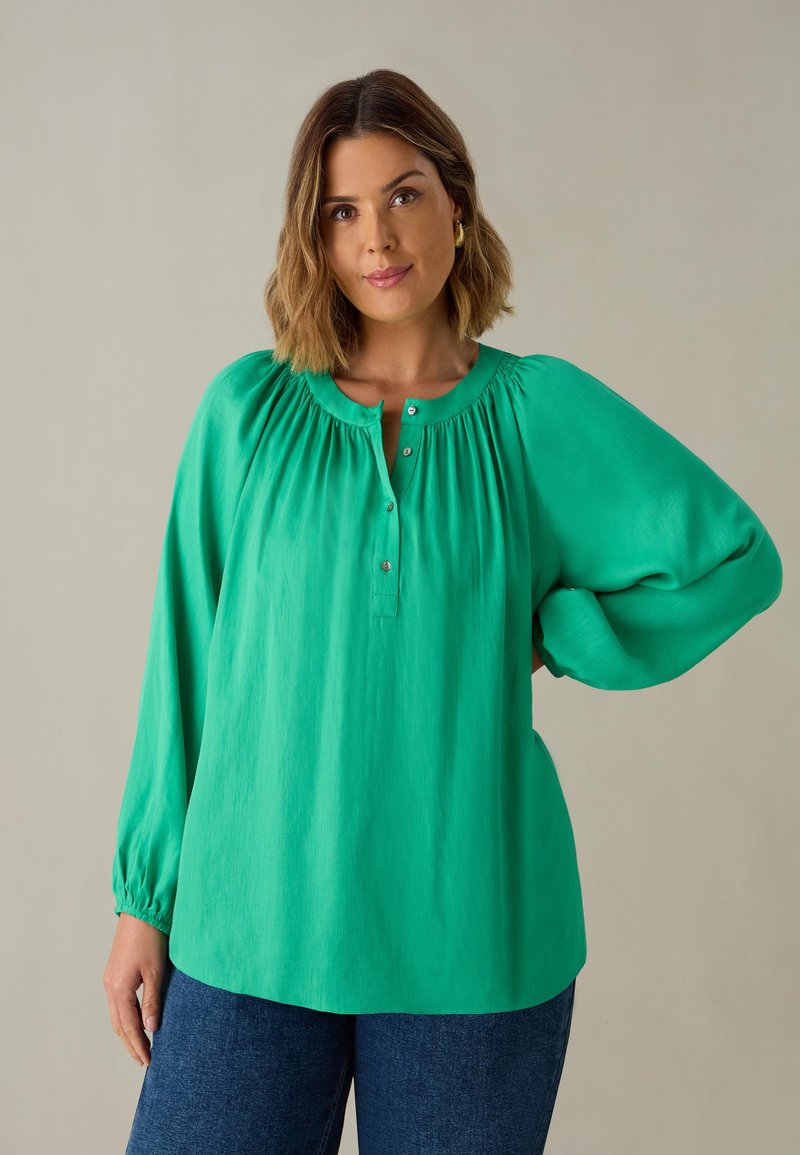 Blusa verde a maniche lunghe con scollatura arricciata, bottoni e polsini elasticizzati. Tessuto morbido, vestibilità rilassata, design fino all'anca.