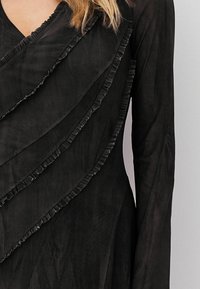 Schwarzes Kleid mit schichten Rüschendetails am Ausschnitt und den Ärmeln, aus einem leichten, strukturierten Stoff und mit fließender Silhouette.