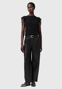 Czarna dopasowana bluzka z dekoracjami z koralików na ramionach, zestawiona z czarnymi, skórzanymi, szerokimi spodniami z wysokim stanem oraz wsuwanymi butami.